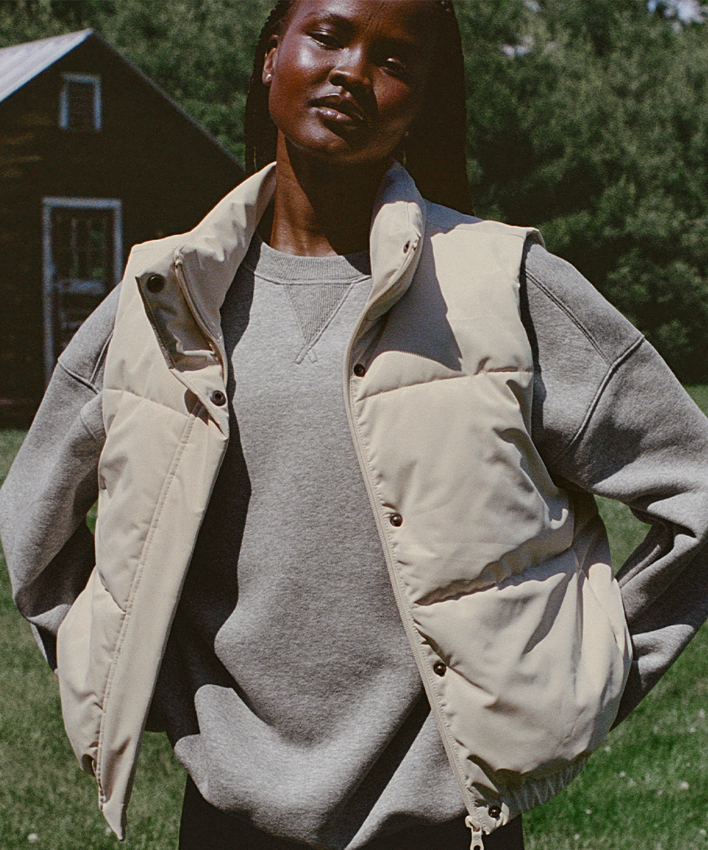 A woman layering a puffer vest over a crewneck sweatshirt.