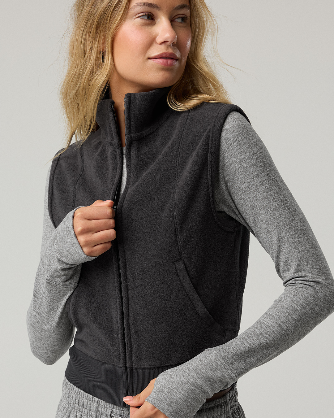 Woman layering black vest over a gray long sleeve shirt.
