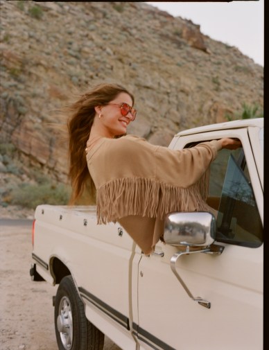Woman wearing Aerie fringe coat in a truck.